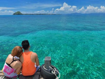 Malaysian couple sitting on a wooden pier looking at the clear turquoise sea and fantastic horizon.